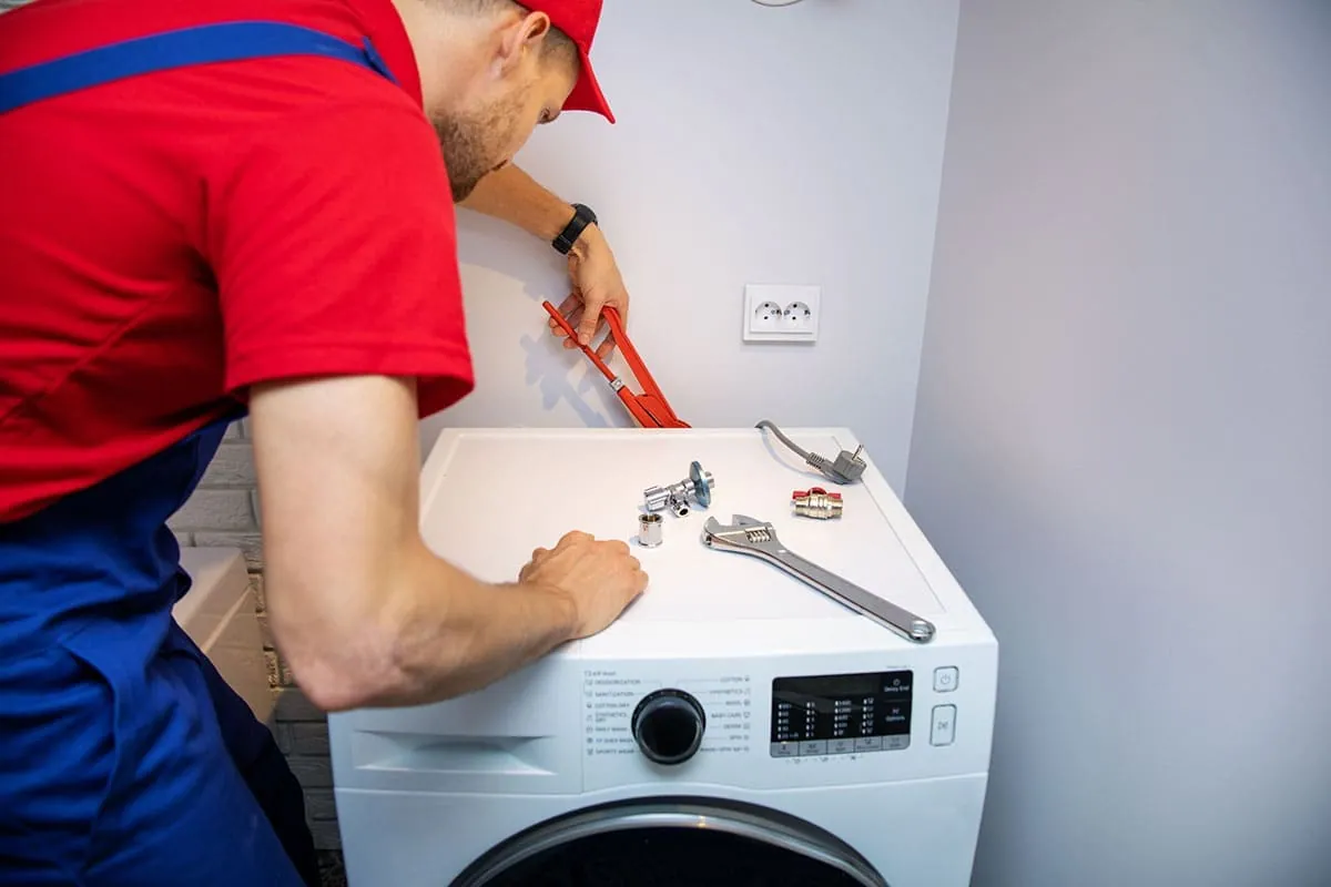 Técnico conectando las tomas de agua y desagüe de una lavadora durante una reparación en Tenerife