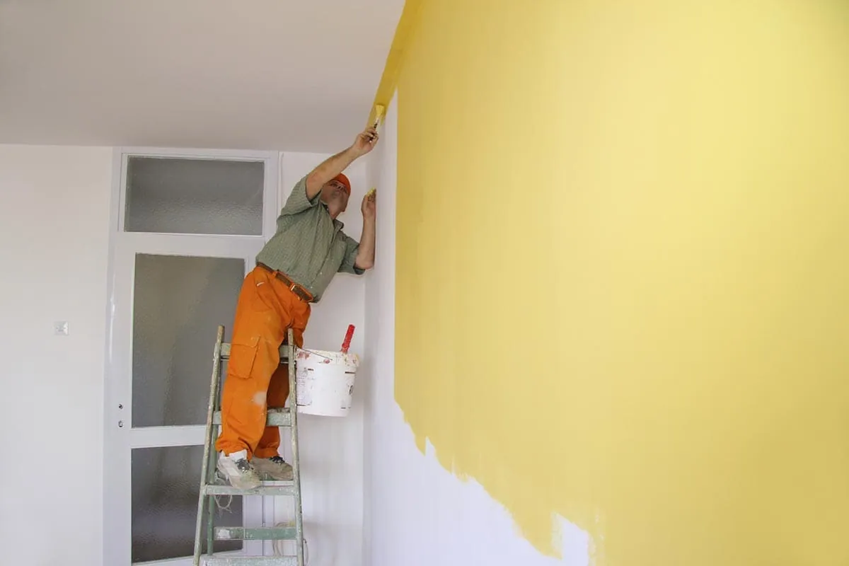 Pintor subido a una escalera pintando una pared de color amarillo en una vivienda de Tenerife