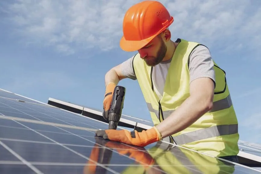 Instalador con casco fijando un panel fotovoltaico a la estructura de una cubierta
