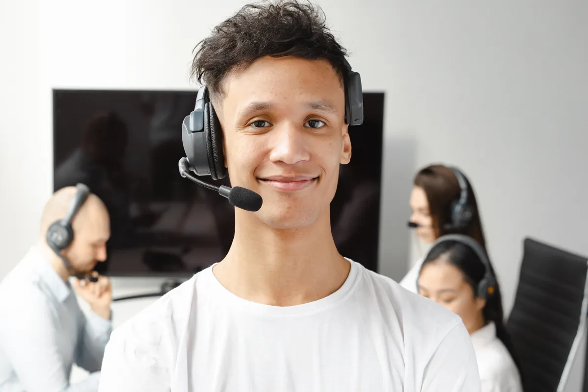 Agente de atención al cliente sonriente, con auriculares y micrófono, en una oficina con compañeros
