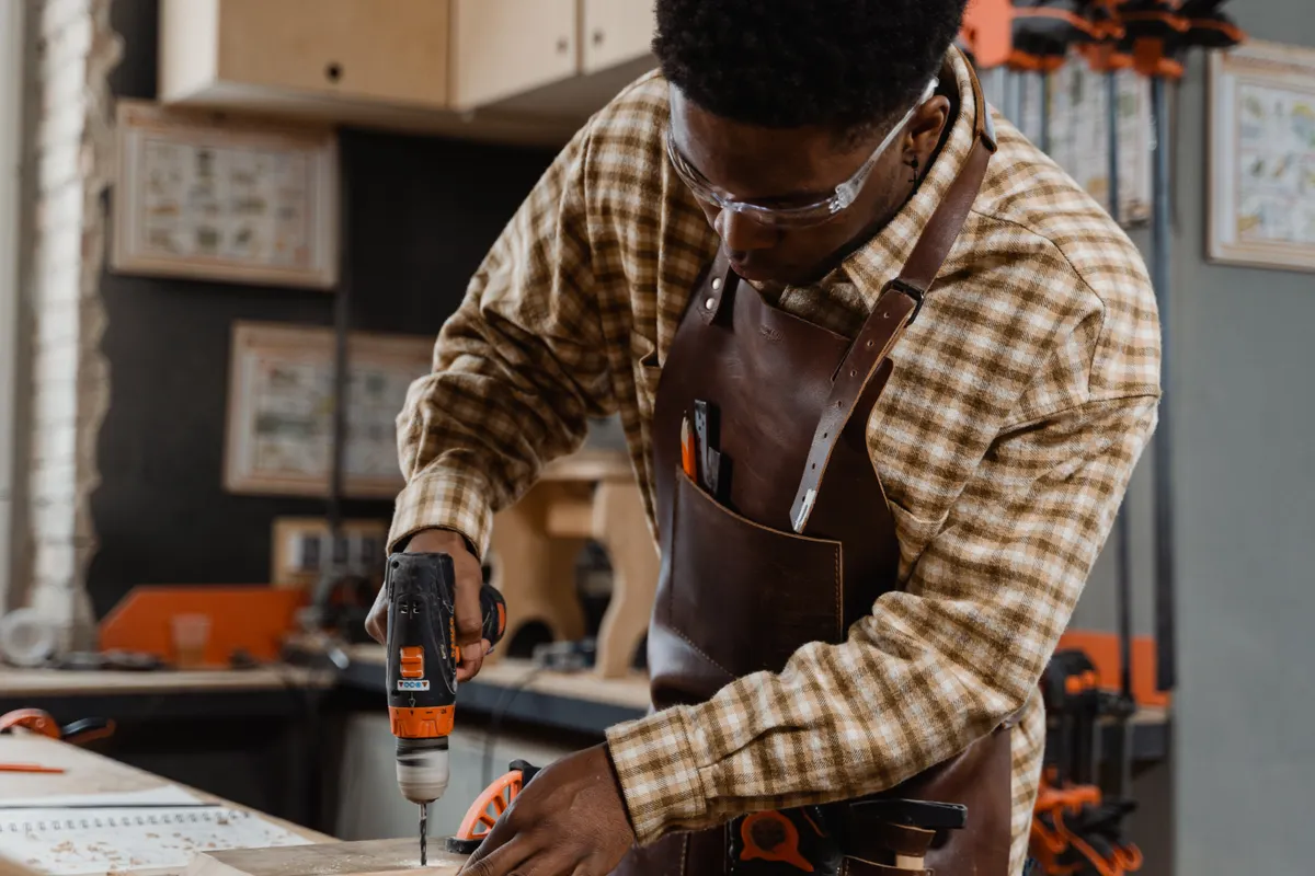 Artesano con gafas de seguridad y delantal trabajando la madera con un taladro eléctrico
