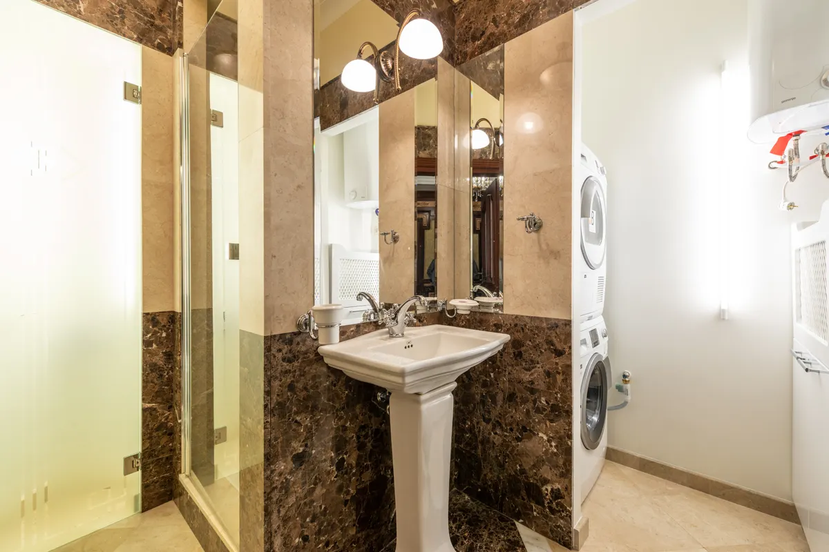 Baño elegante con paredes de mármol, lavabo de pie y lavadora secadora