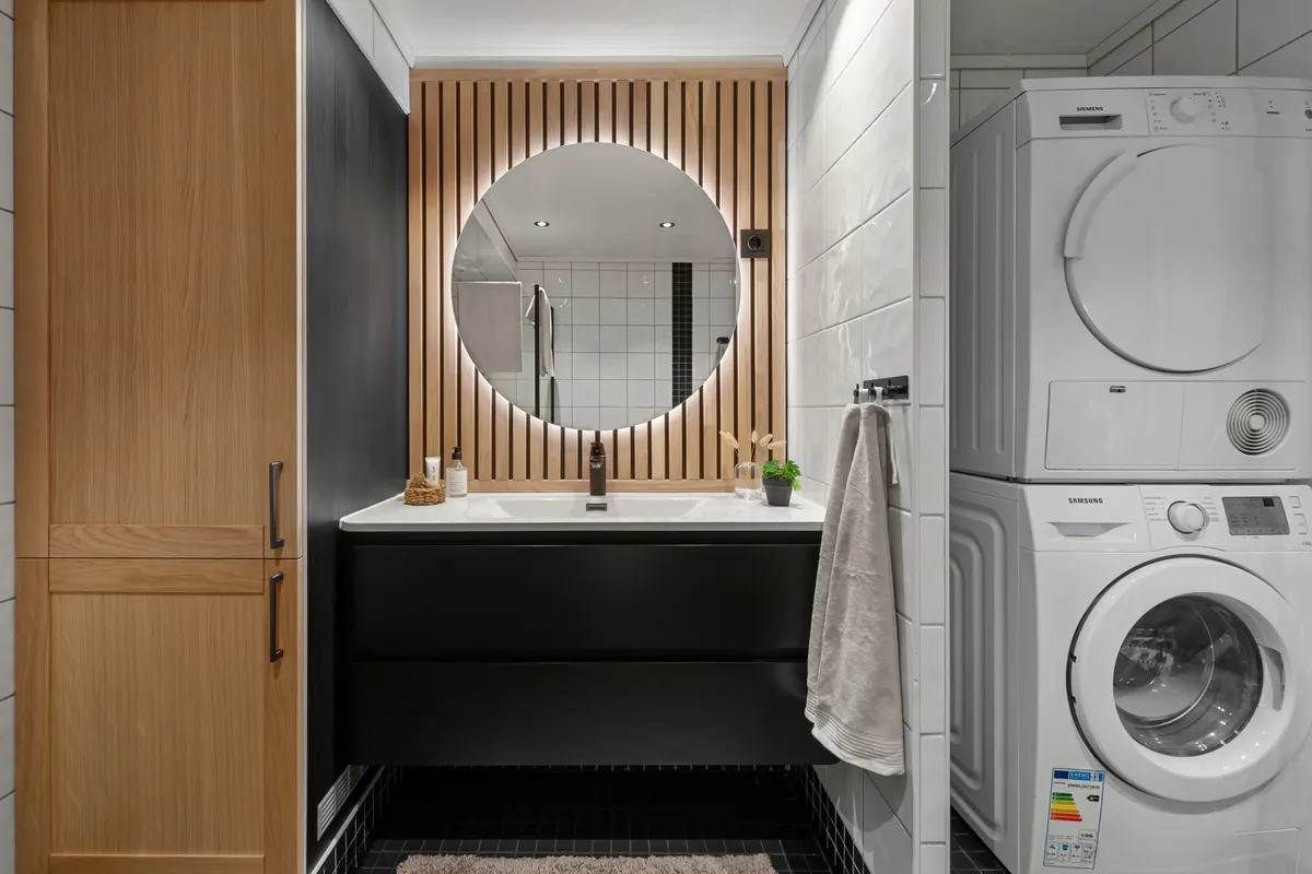Baño moderno con espejo redondo, lavabo y lavadora y secadora integradas