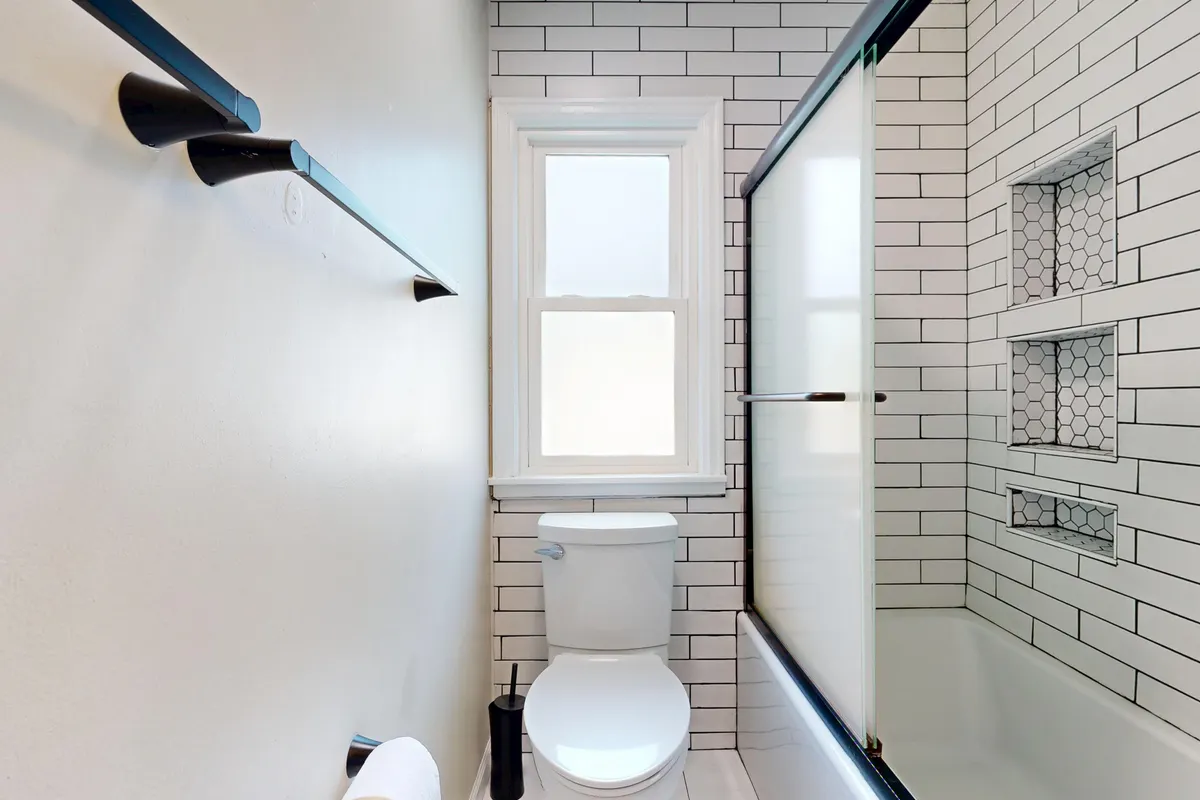 Baño moderno y bien iluminado con azulejos blancos tipo metro y un inodoro