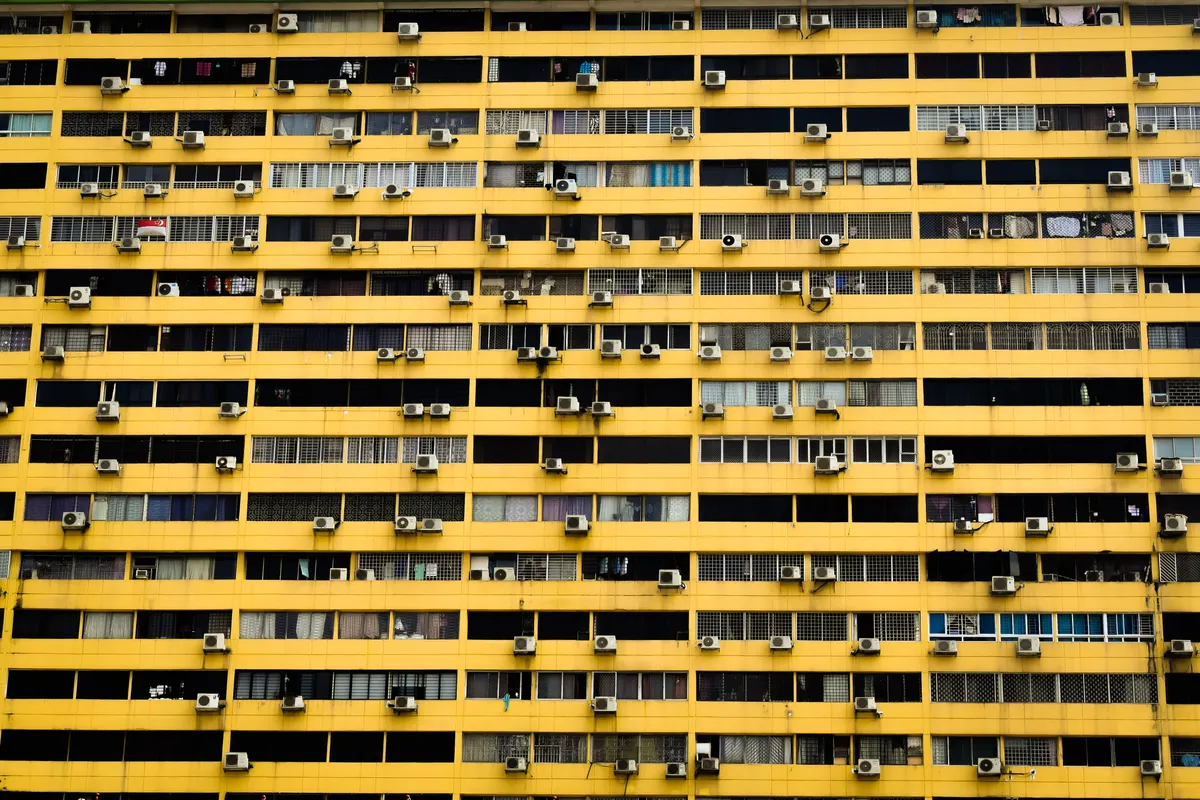 Bloque de pisos amarillo visto desde abajo con muchos aparatos de aire acondicionado