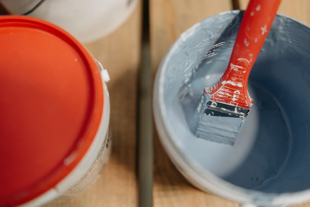 Brocha roja mojada en un cubo de pintura azul, lista para pintar