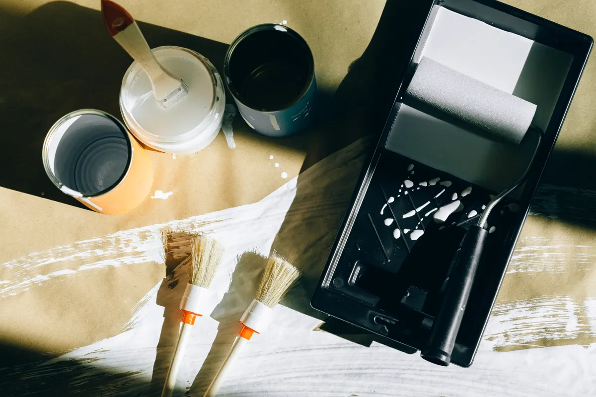 Brochas, rodillos y botes de pintura sobre papel vistos desde arriba