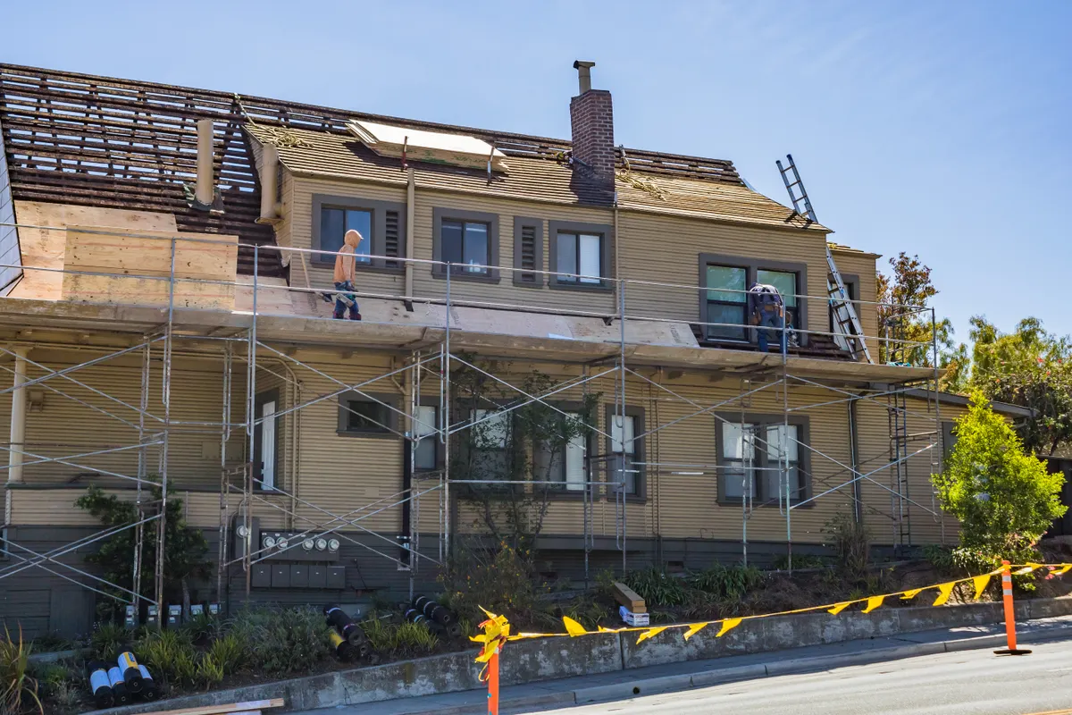 Casa en obras con andamios y operarios arreglando el tejado en un día soleado