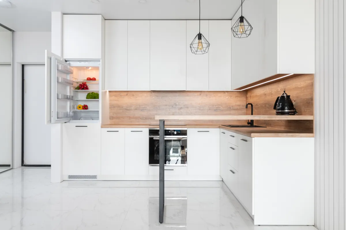 Cocina blanca con el frigorífico integrado abierto y verduras frescas en sus baldas