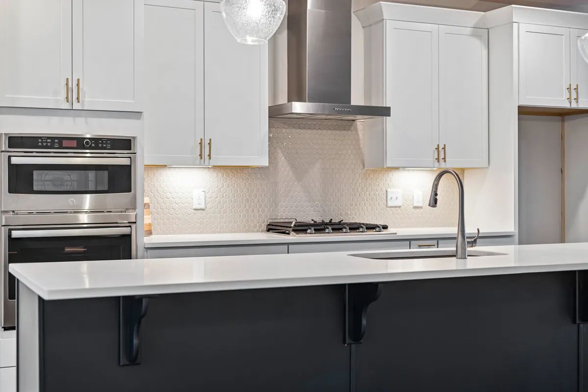 Cocina moderna con muebles blancos, horno empotrado, fogones e isla central con fregadero