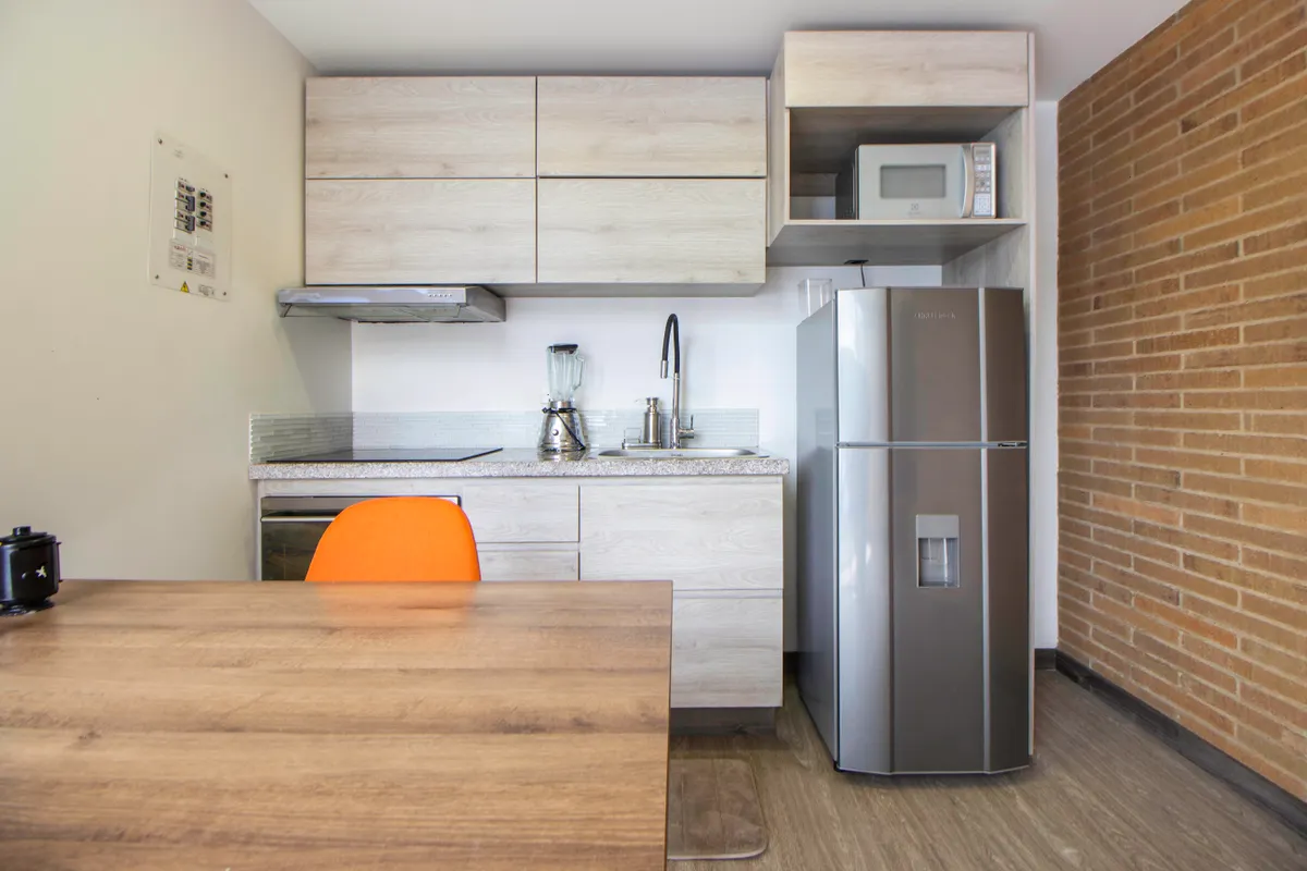 Cocina moderna con muebles de madera, electrodomésticos de acero y una silla naranja