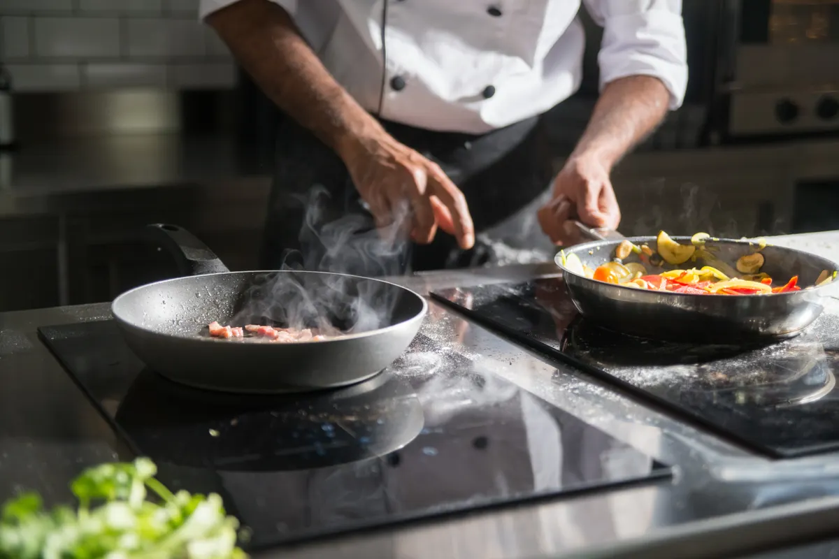 Cocinero preparando un plato con ingredientes frescos en una placa eléctrica