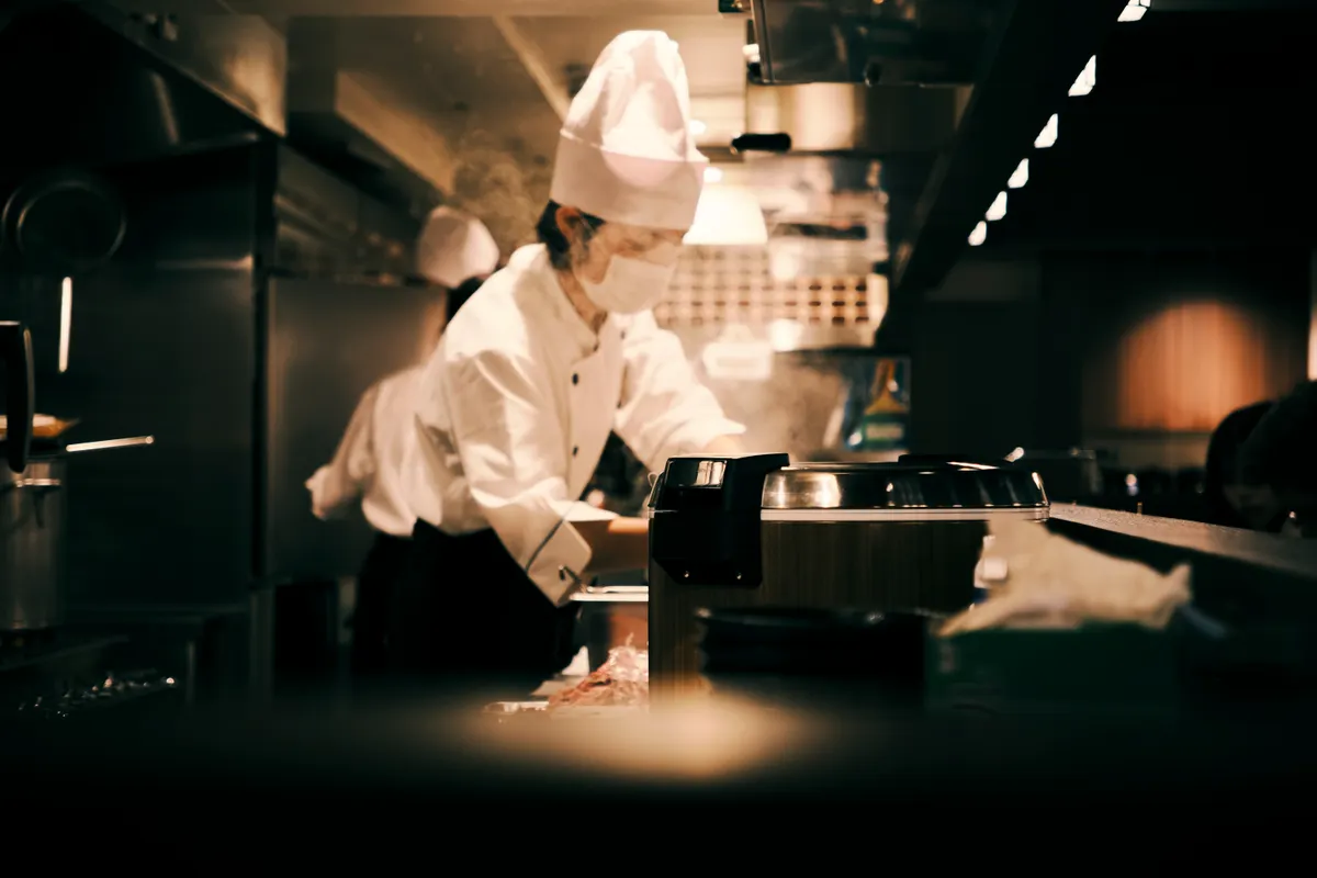 Cocinero uniformado trabajando en una cocina de restaurante con mucho movimiento