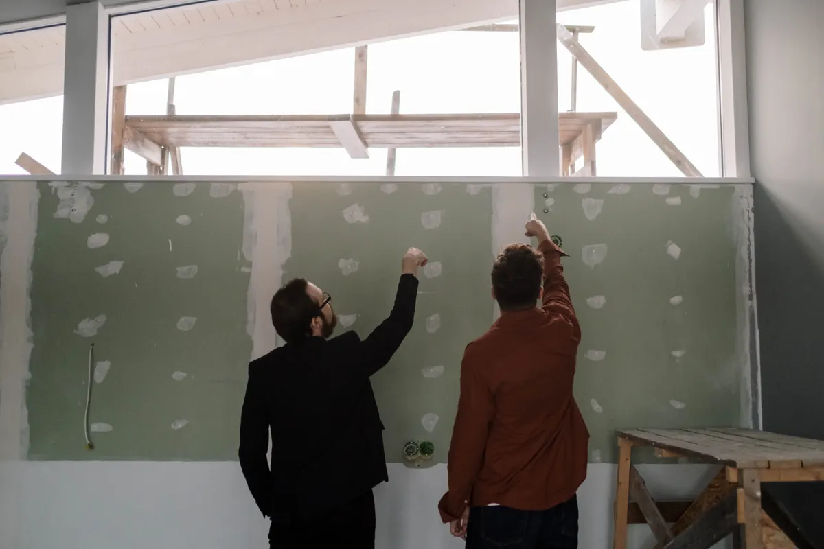 Dos hombres comentando y señalando una pared interior durante una reforma
