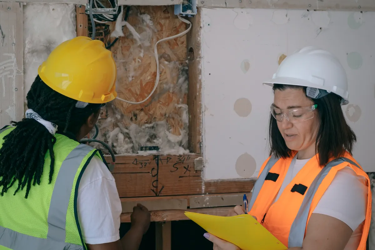 Dos trabajadores con equipo de protección tomando notas durante una inspección eléctrica en una obra