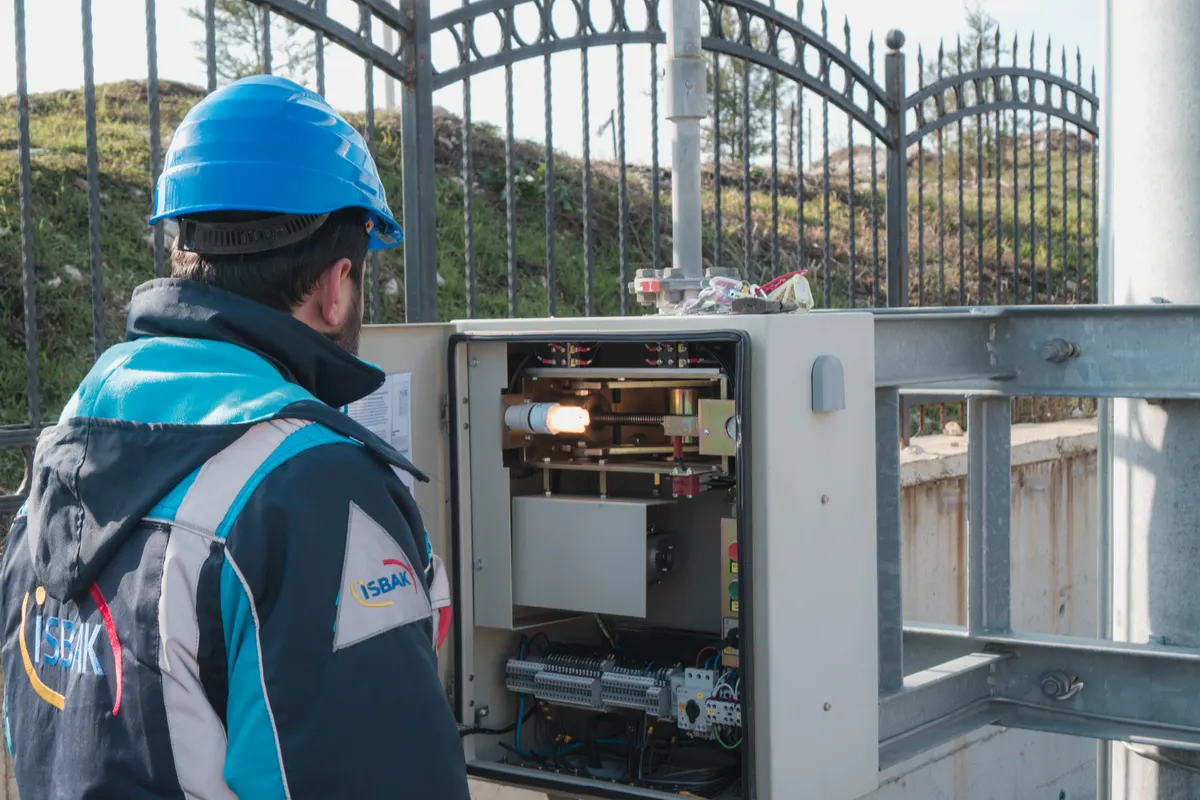 Electricista con casco inspeccionando una caja de fusibles en el exterior