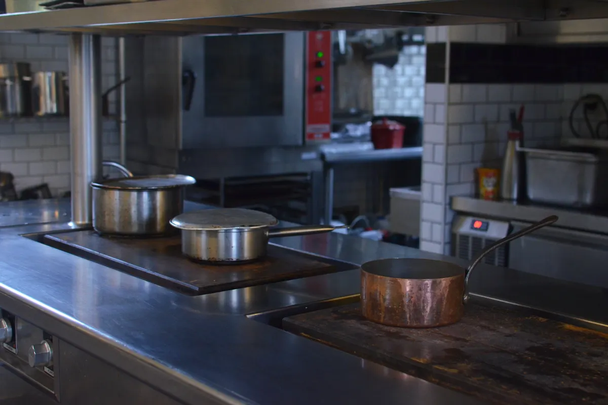 Encimera de acero de una cocina profesional con cazos y equipos al fondo