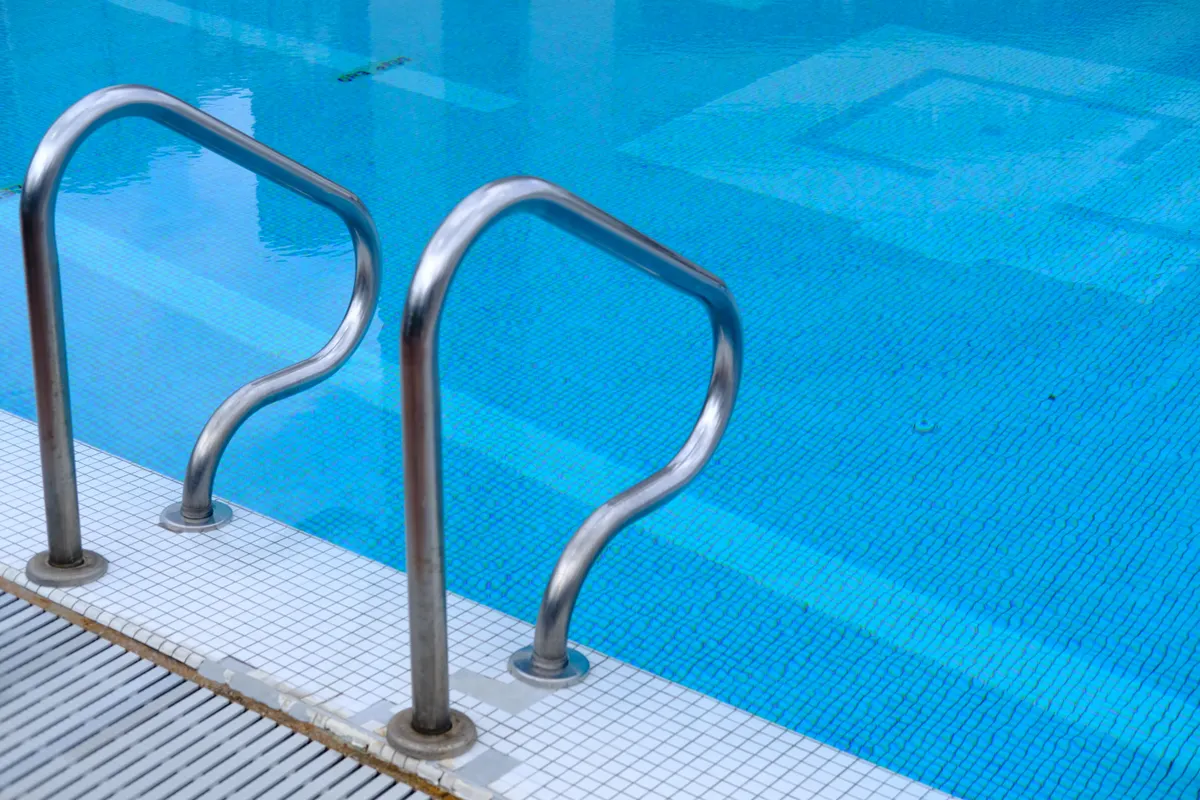 Escalerilla de acero inoxidable que baja a una piscina de azulejo azul