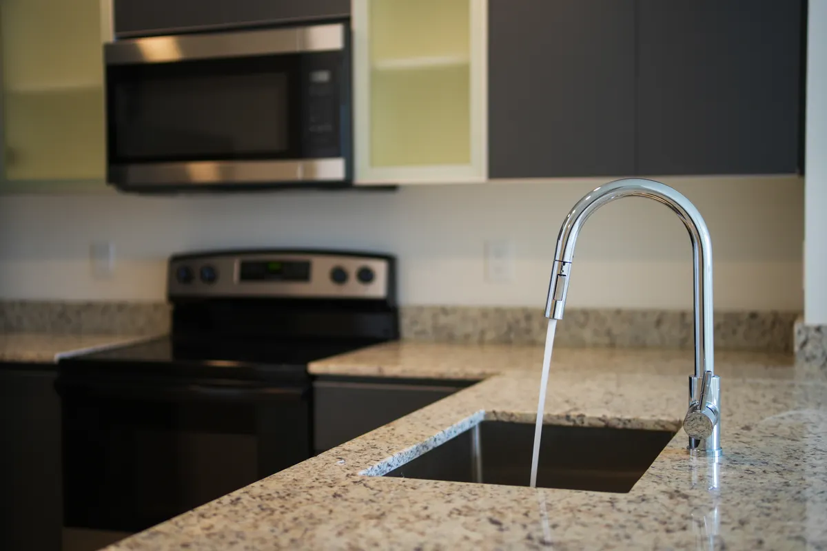 Grifo de cocina sobre una encimera de granito con electrodomésticos modernos a la vista