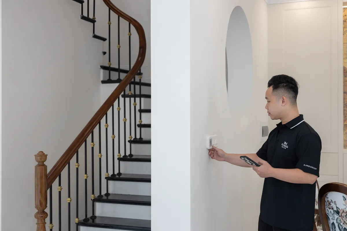 Hombre ajustando el termostato en una casa con una elegante escalera