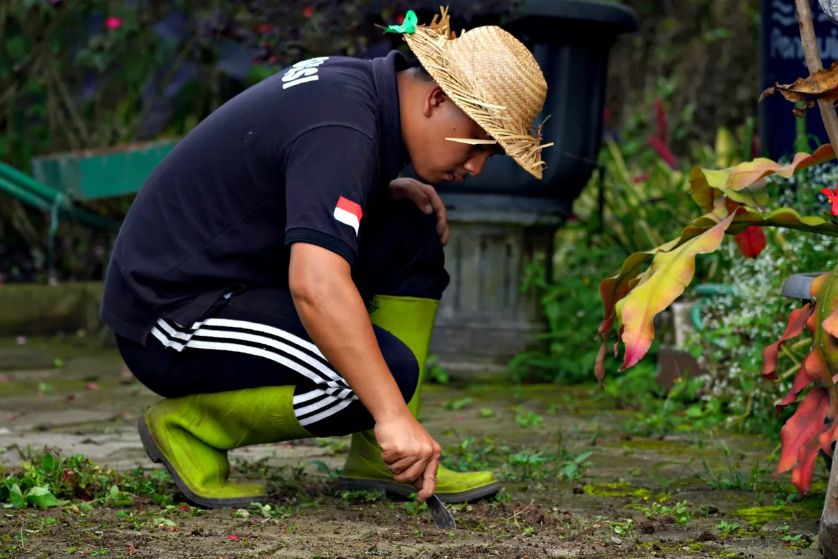 Hombre con botas verdes y sombrero de paja cuidando las plantas del jardín