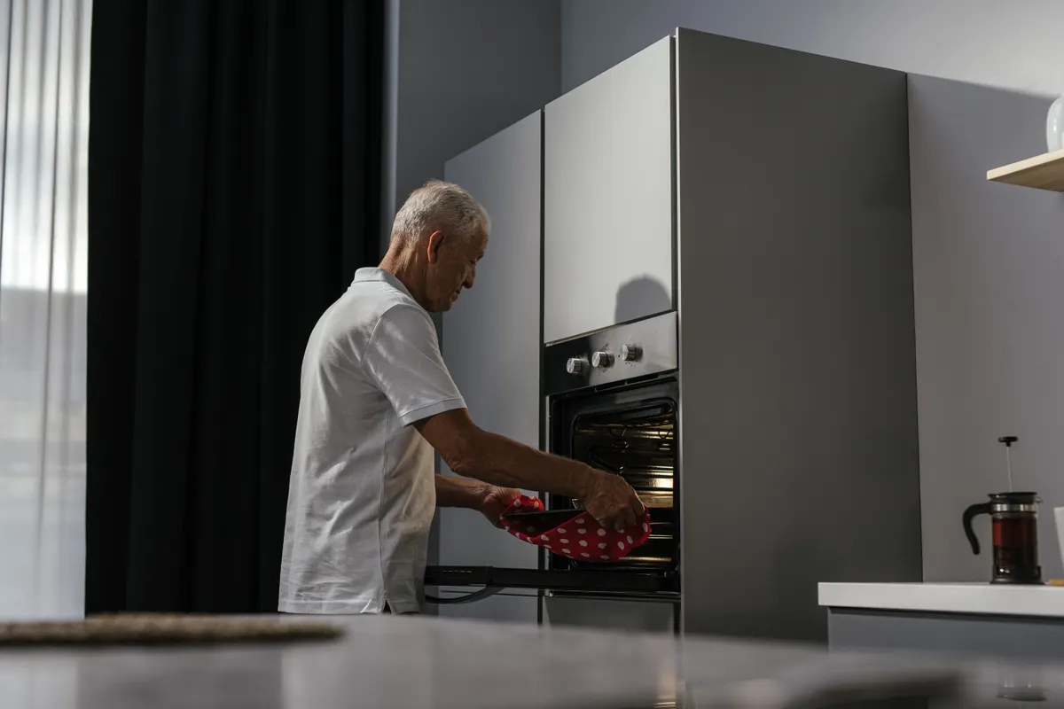 Hombre mayor usando el horno en una cocina moderna con juego de luces y sombras