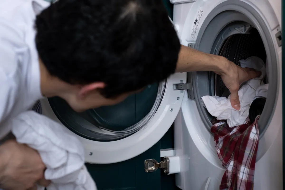 Hombre metiendo ropa en la lavadora durante las tareas de casa