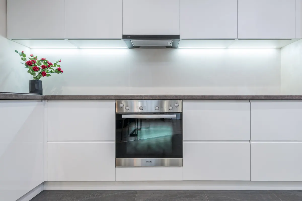 Horno empotrado y campana cromados en una cocina amplia con muebles blancos y un jarrón de flores