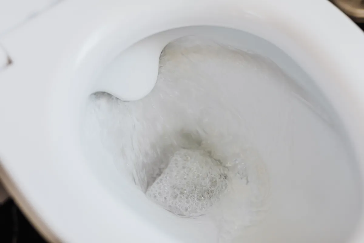 Inodoro blanco de cerámica con el agua de la cisterna corriendo, visto desde arriba