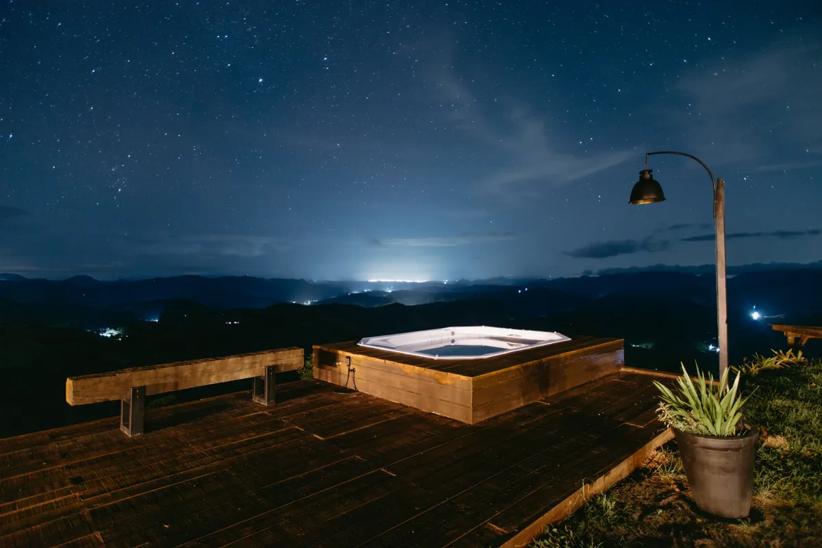 Jacuzzi exterior bajo un cielo estrellado con las luces de una ciudad a lo lejos