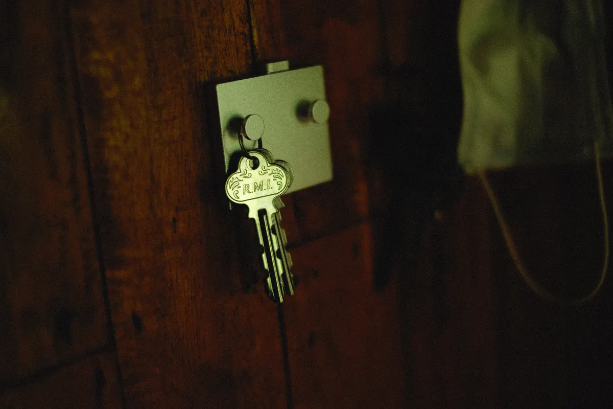 Llave metálica marcada con unas iniciales, colgada de un gancho rústico de madera en la pared