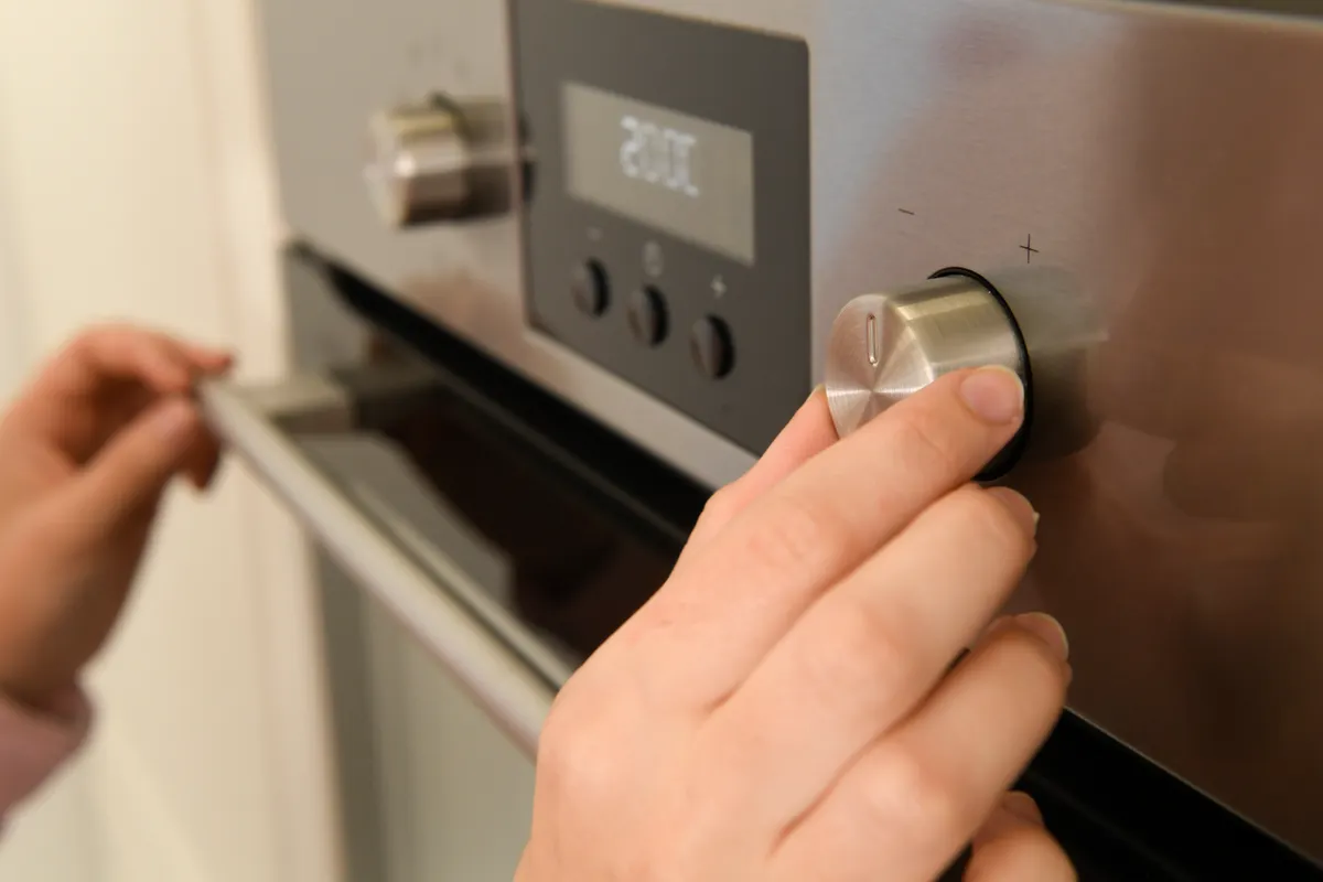 Mano girando el mando de temperatura de un horno eléctrico empotrado de acero inoxidable con pantalla digital