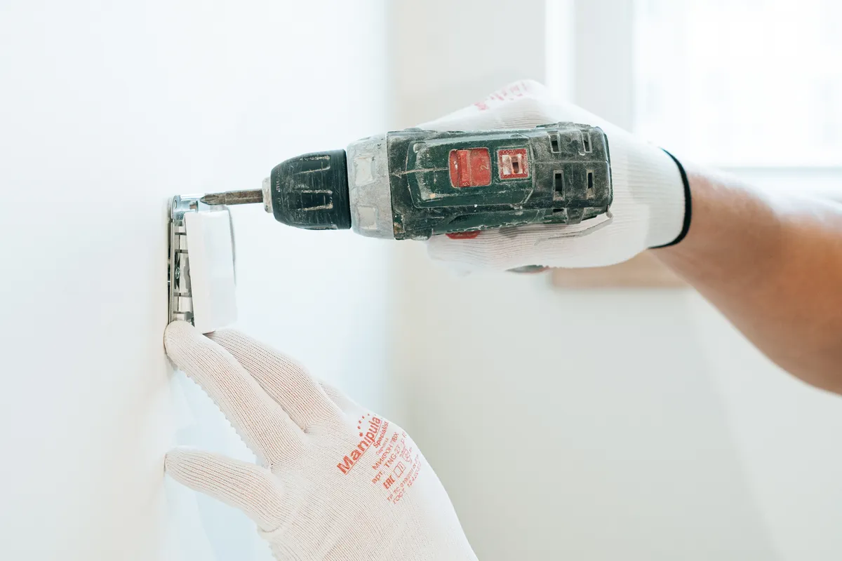 Manos con guantes usando un taladro para instalar un enchufe en la pared