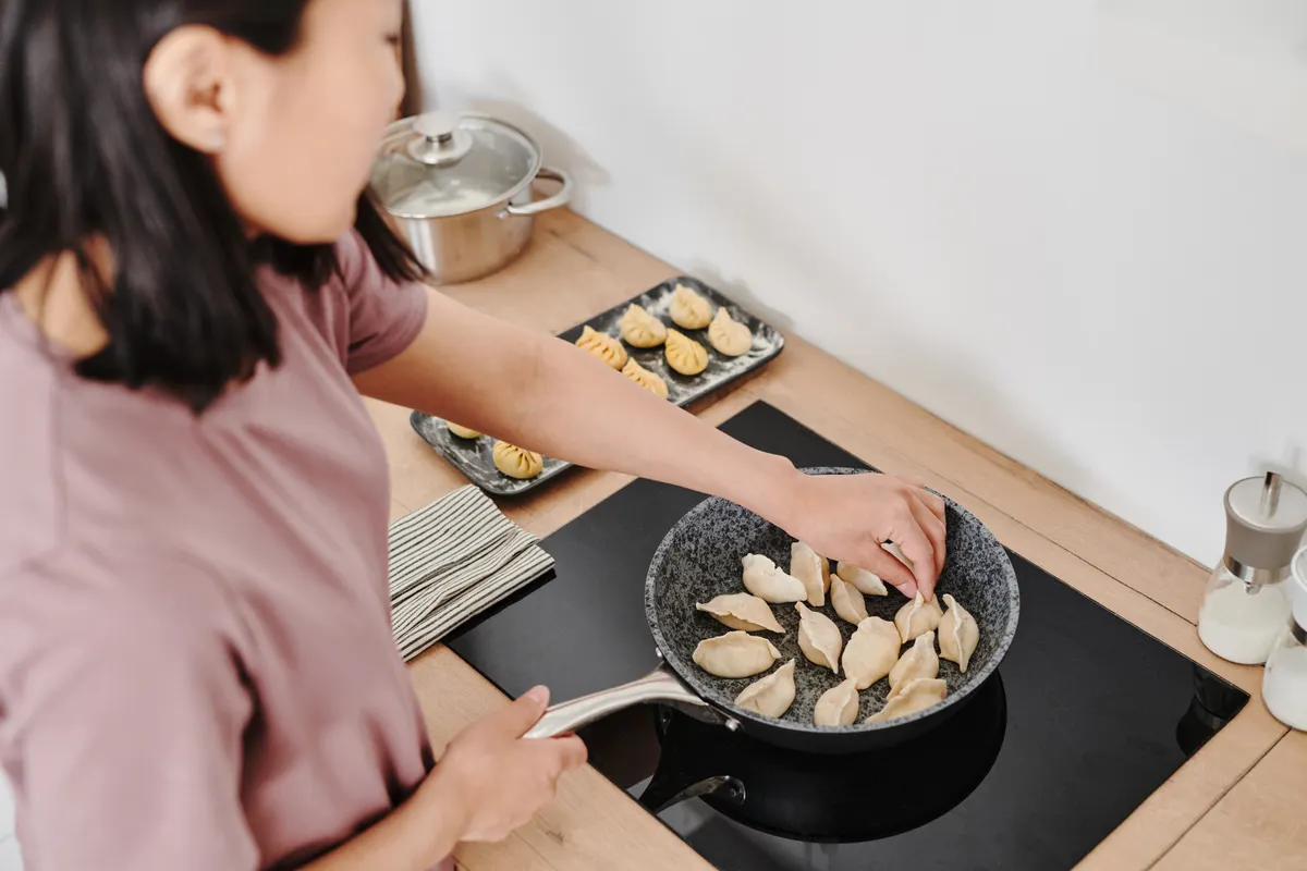 Mujer cocinando dumplings en la placa de una cocina moderna