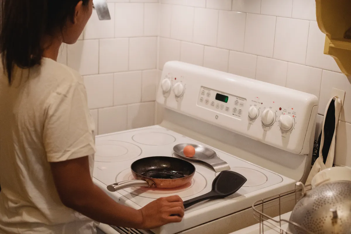 Mujer con camiseta blanca junto a la placa a punto de preparar huevos revueltos