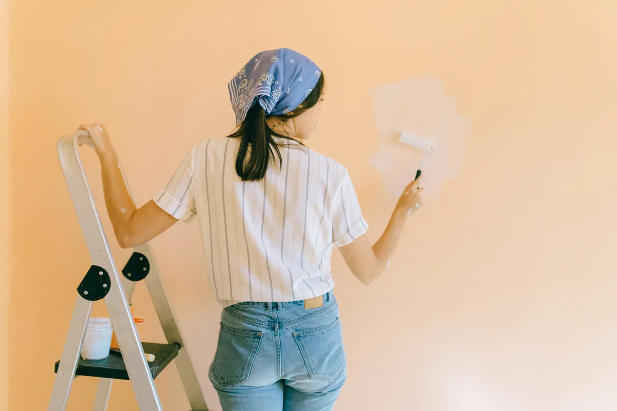 Mujer con un pañuelo pintando con rodillo una pared de color melocotón