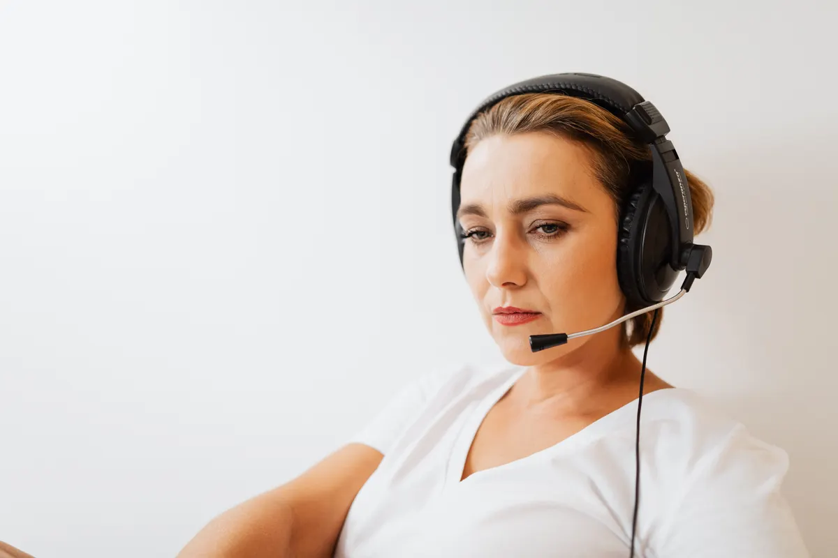 Mujer concentrada con auriculares atendiendo a clientes sobre un fondo blanco