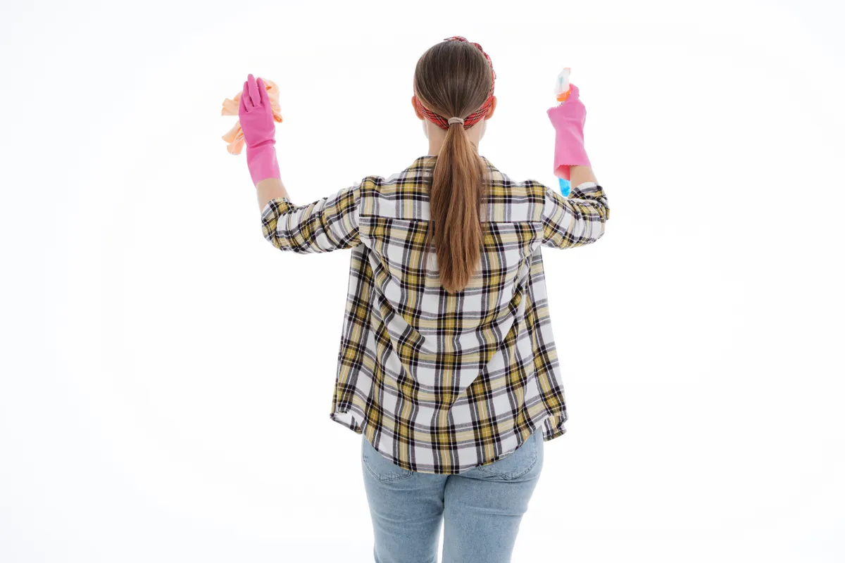 Mujer de espaldas con guantes de látex limpiando con un espray y un paño