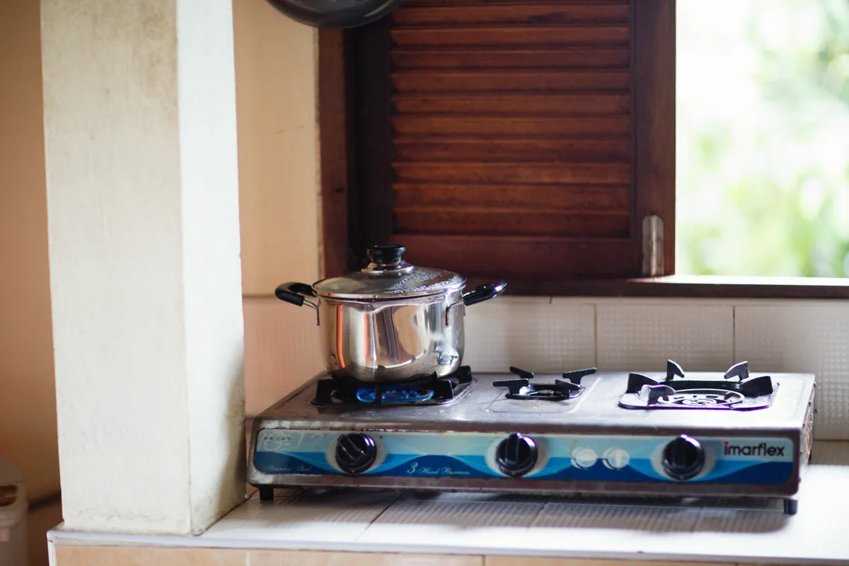 Olla de acero inoxidable sobre una cocina de gas encendida junto a una ventana con contraventanas de madera