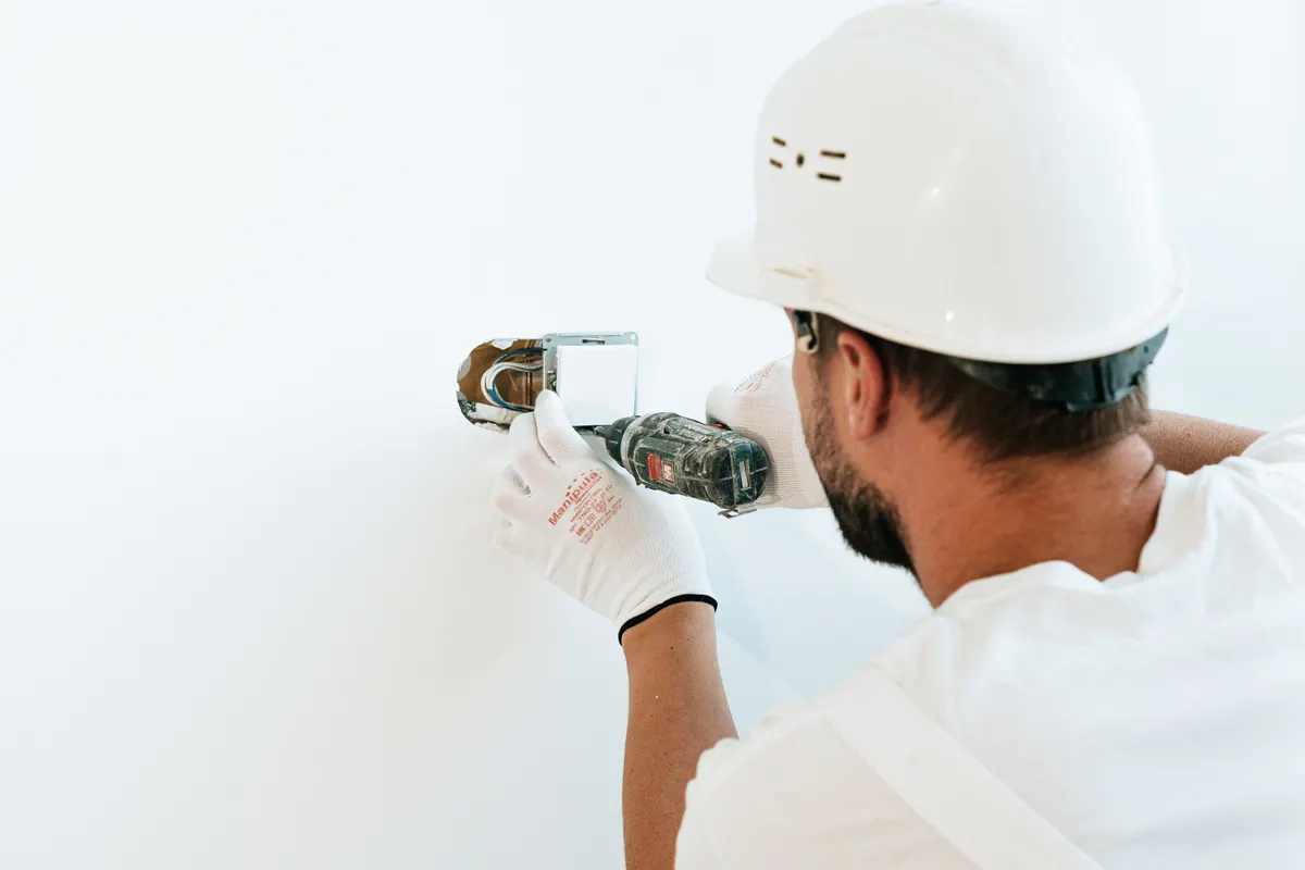 Operario con casco y guantes reparando una pared con una herramienta eléctrica