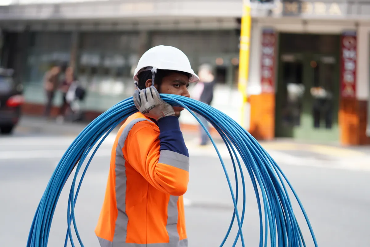 Operario con equipo de seguridad cargando cables azules en una calle de la ciudad
