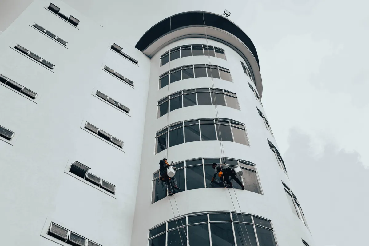 Operarios limpiando con cuerdas las ventanas de un edificio alto y moderno