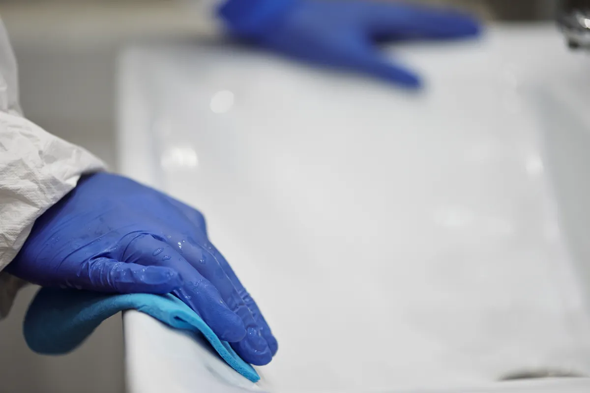 Persona con guantes desinfectando el lavabo del baño con un paño