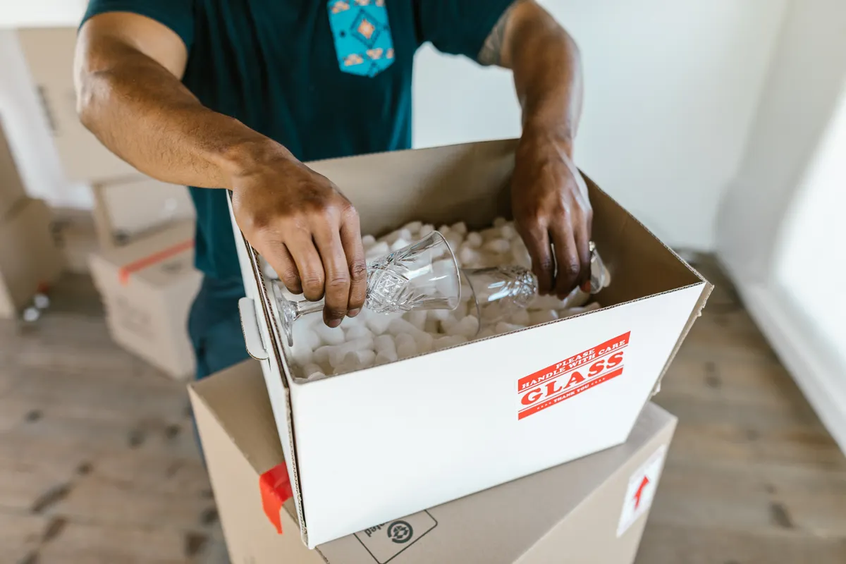 Persona embalando cristalería en cajas con relleno de poliestireno para la mudanza