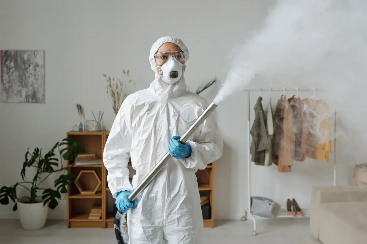 Profesional con mono, gafas y mascarilla aplicando una nebulización en el salón de una vivienda