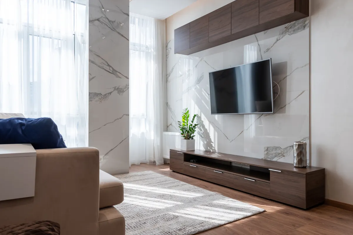 Televisor moderno colgado entre muebles de madera frente a un sofá en un salón luminoso