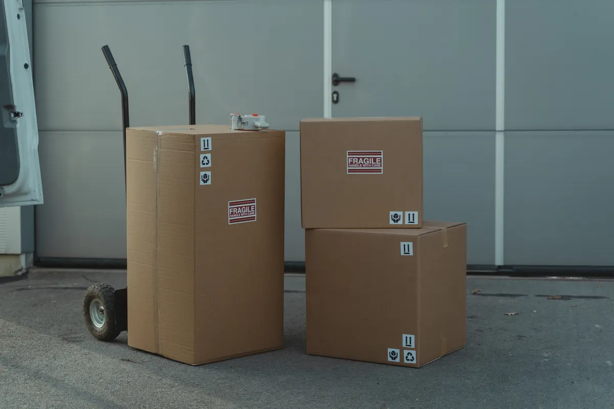 Tres cajas de cartón sobre una carretilla de mano listas para el envío junto a un almacén