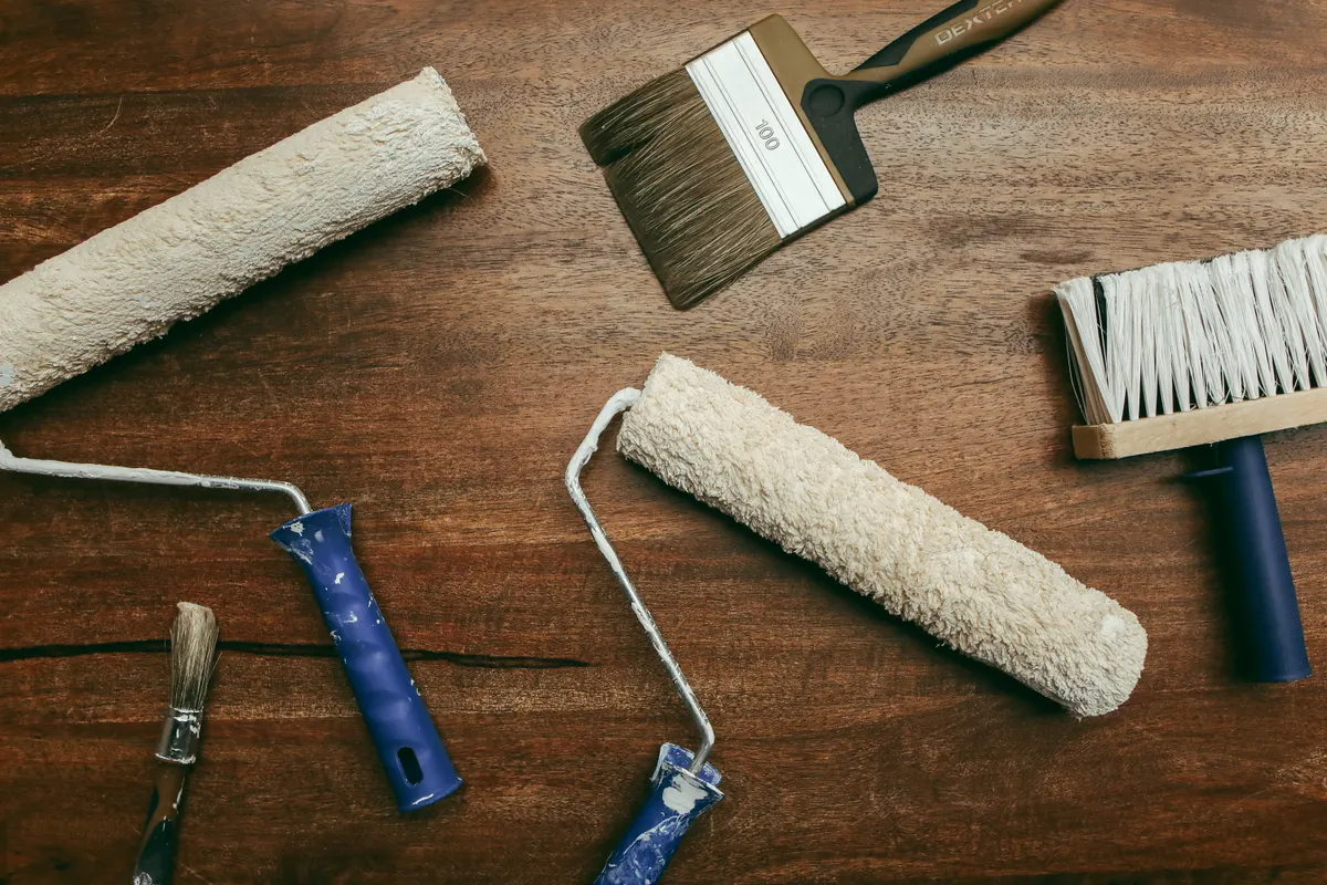 Vista cenital de rodillos, brochas y otras herramientas de pintura sobre una superficie de madera